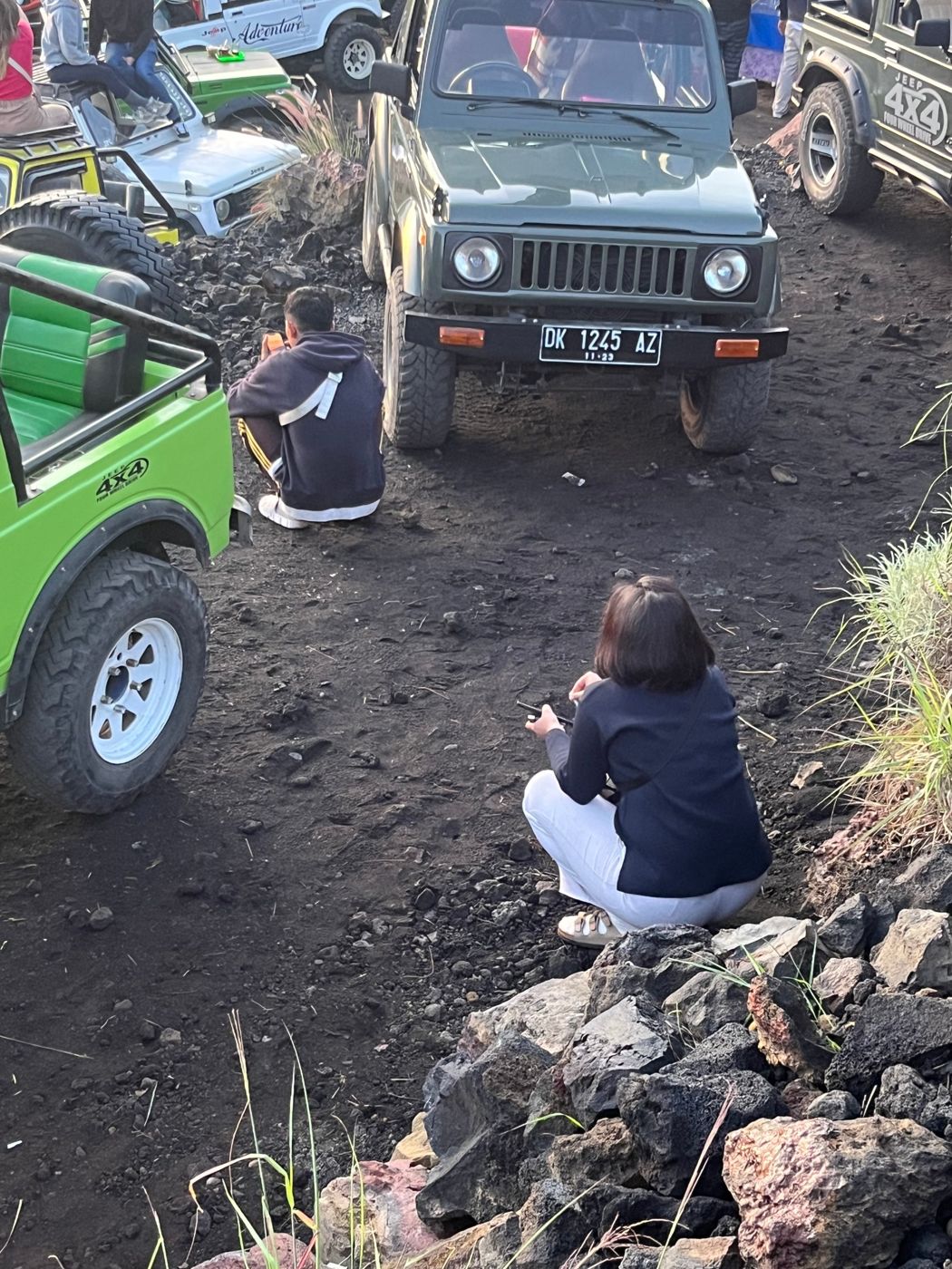 Two people sitting in a deep squat beside jeeps in Bali