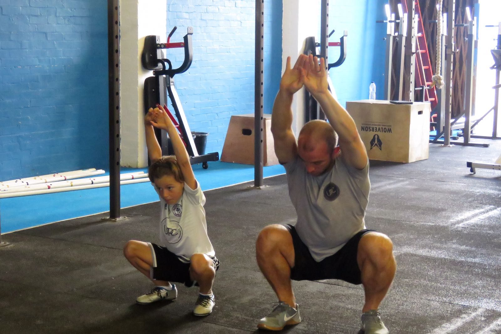 Gavin and Jude squatting together in the gym, arms overhead